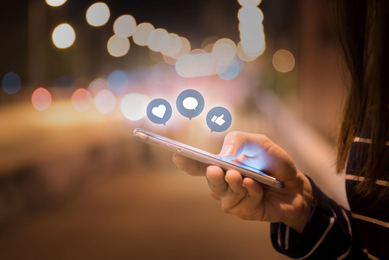 Smartphone mit Social-Media-Symbolen vor Lichtern der Stadt